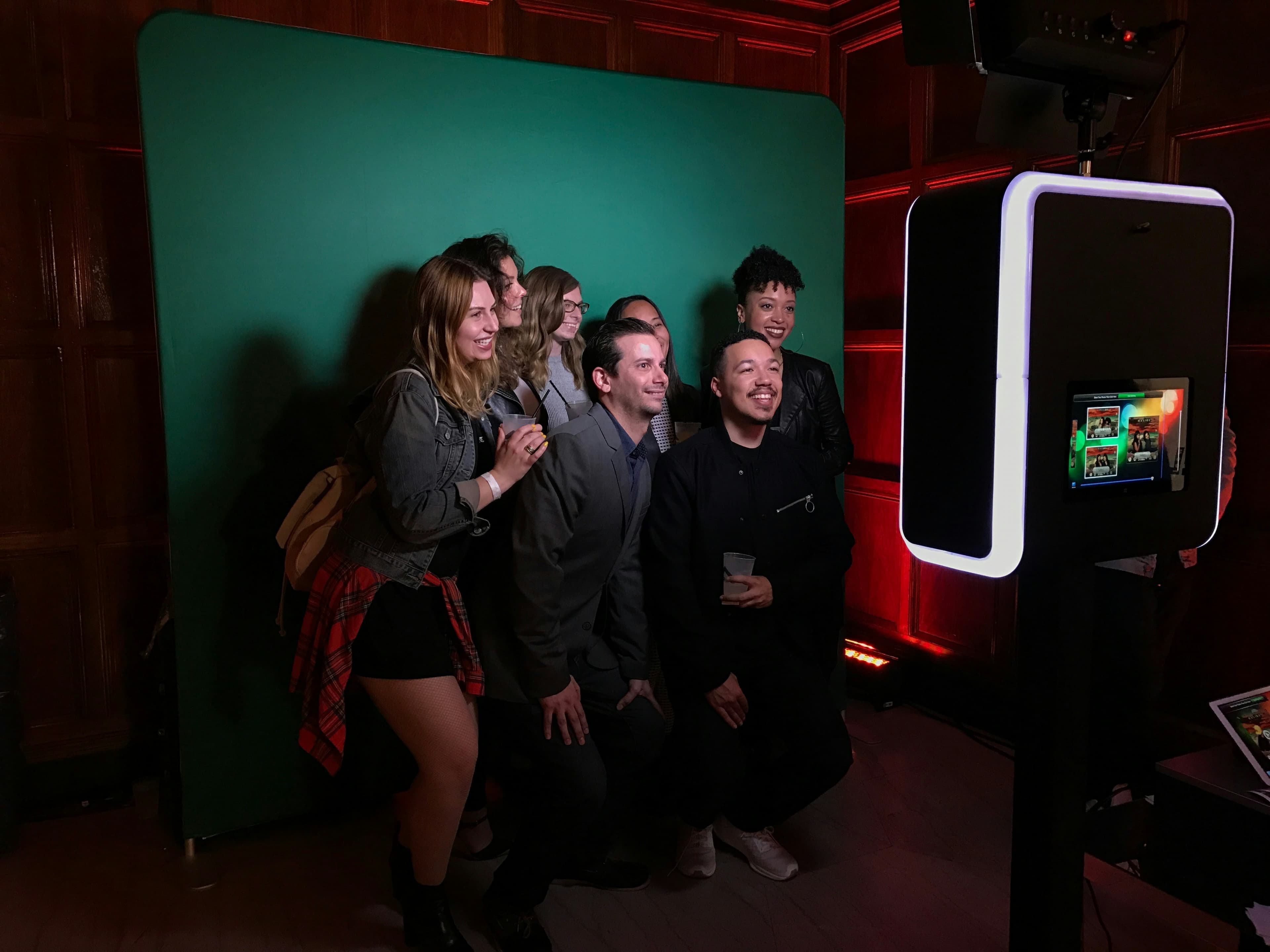Group of friends posing with fun props in illuminated photo booth with neon backdrop
